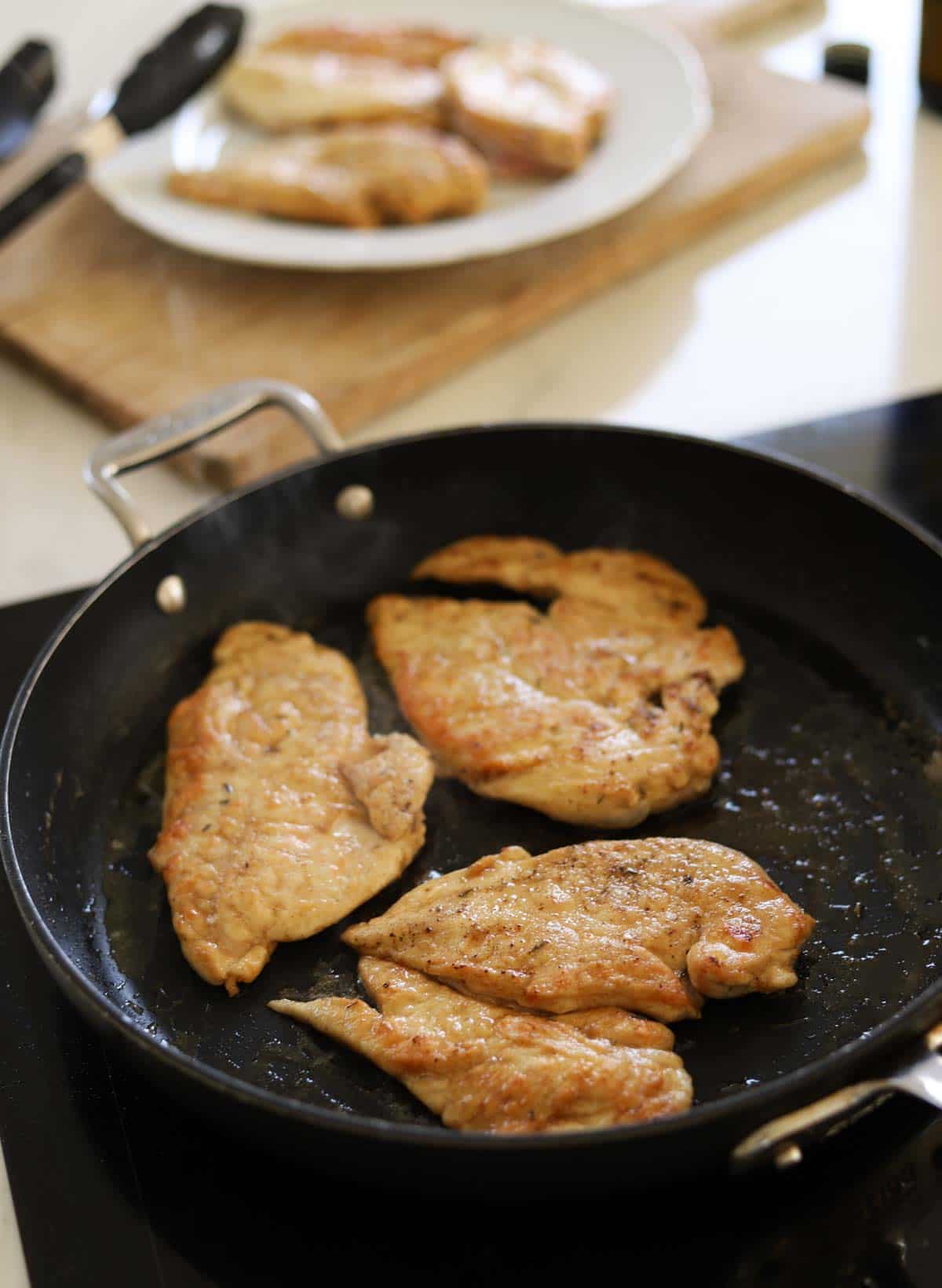 Chicken breasts searing in a nonstick pan.