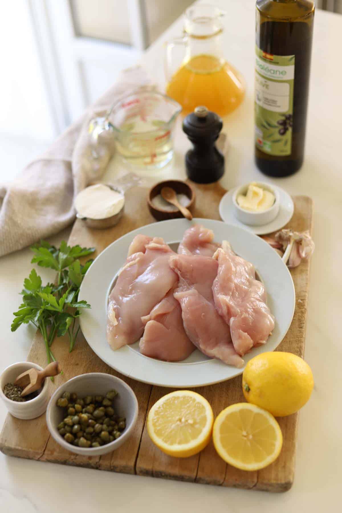 chicken, lemon, caperts, butrter, wine, chicken broth and other ingredients on a counter.