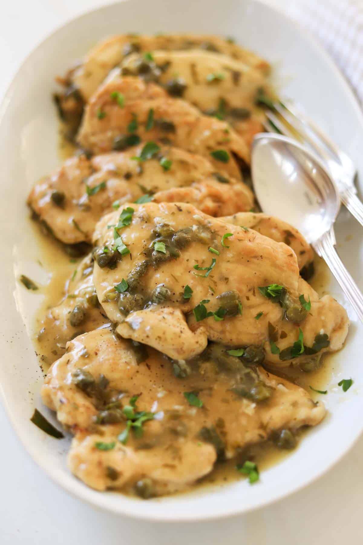 a platter of seared chicken breast, capers, and a lemon butter sauce, garmished with parsley.
