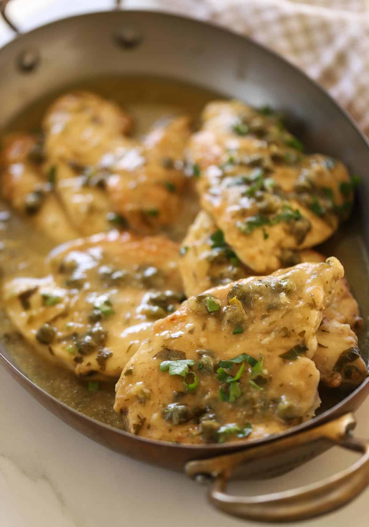 Chicken piccata in a gratin pan covered in capers and fresh parsley garnish.