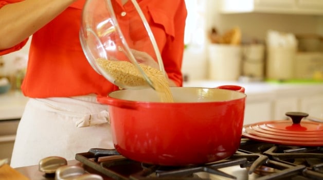 Pouring glass bowl of oatmeal to large pot on stove