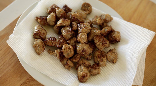 browned Italian sausage draining on a plate lined with paper towels