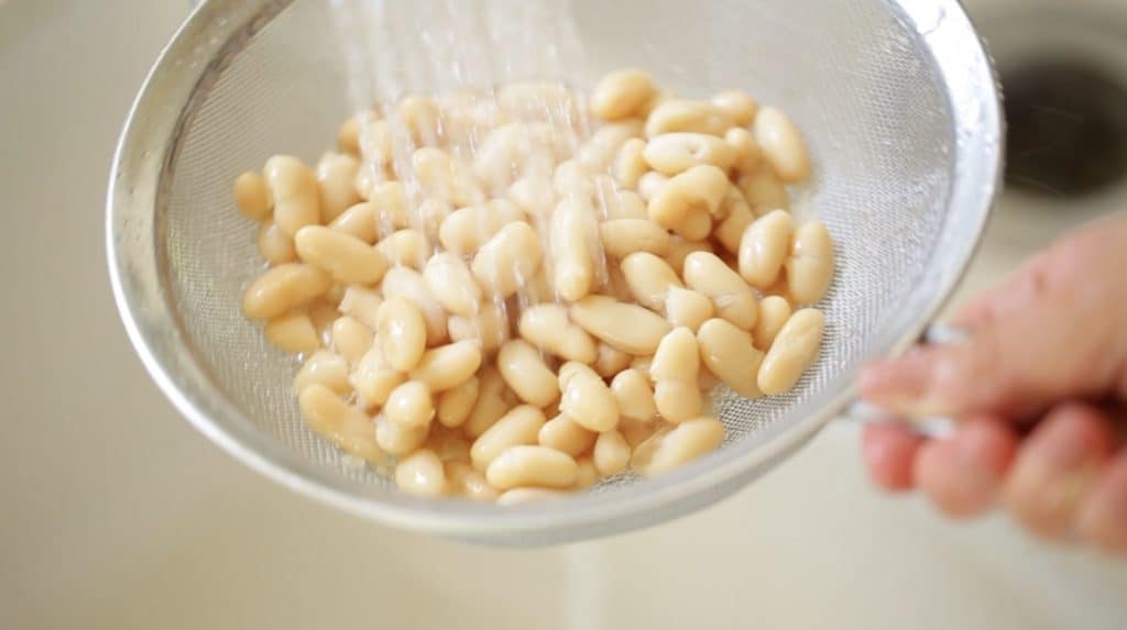 Rinsing white beans in a strainer under a faucet