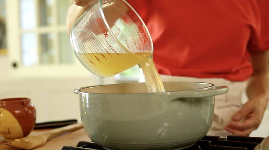 pouring chicken broth from a pitcher into a dutch oven