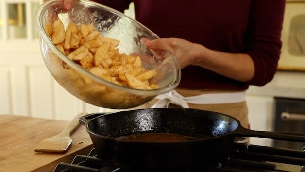 adding apples to a cast iron skillet from a large clear bowl