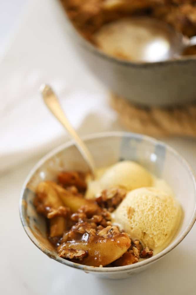 A small bowl of vanilla ice cream topped with warm apple crisp.