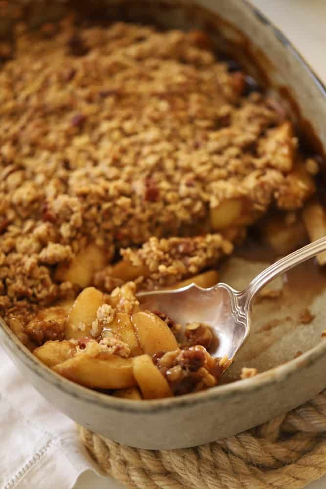 A close up shot of a serving spoon scooping out a spoonful of apple crisp.
