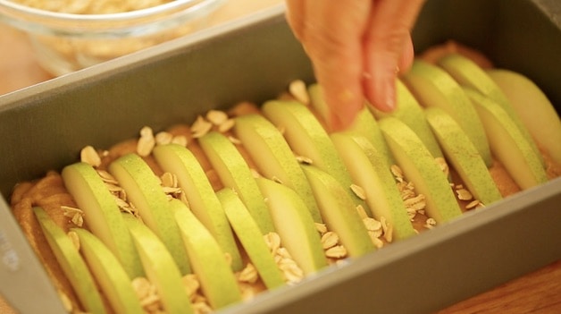 Placing oats on top of cake in loaf pan topped with pears ready for the oven 