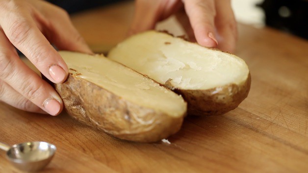 Holding open a sliced baked potato on a cutting board