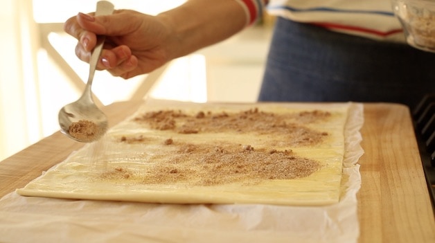 sprinkling cinnamon sugar filling to a puff pastry sheet