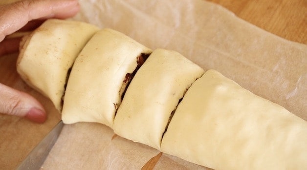 slicling a sticky bun dough log into thirds