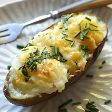 Twice Baked Potato on a white plate garnished with Cheese and Chives