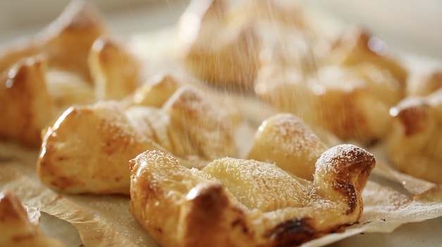 Apple Pastries on baking sheet being dusted with powdered sugar