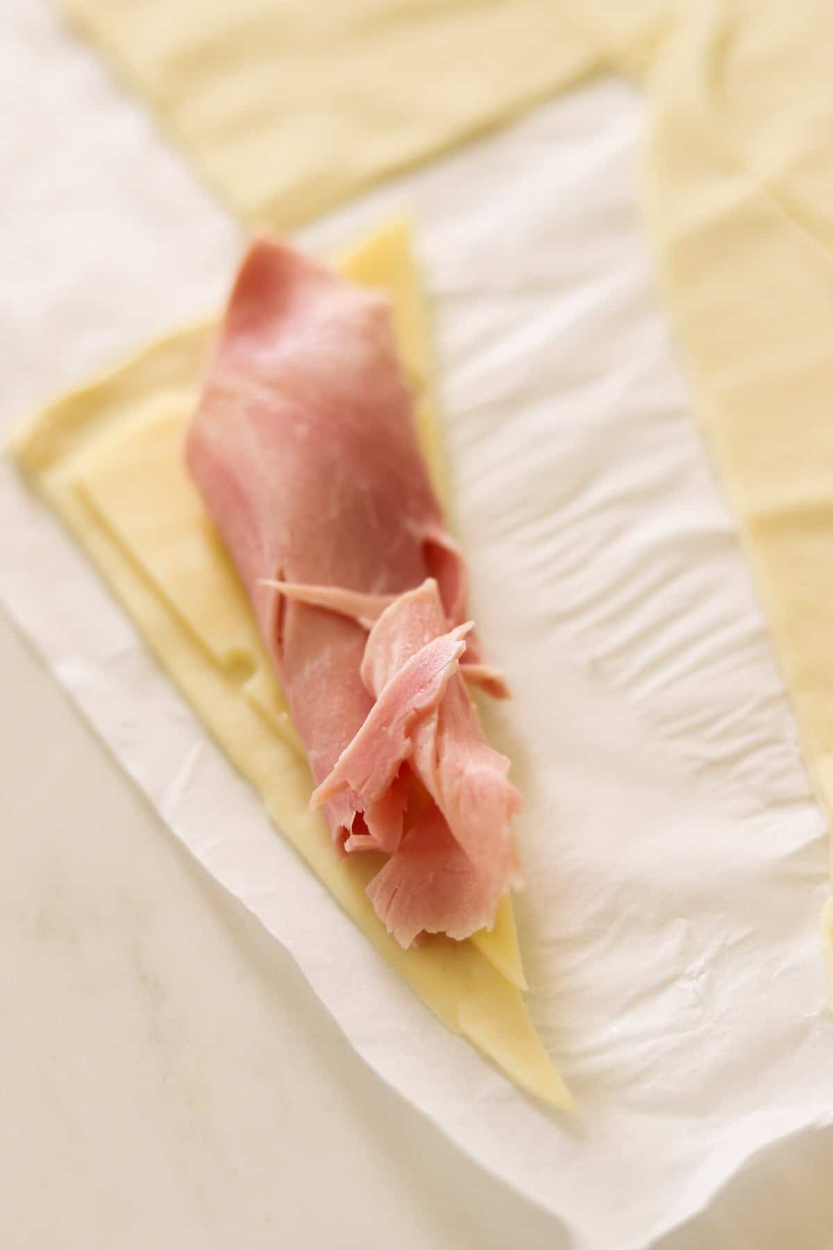 Cheese and ham on a puff pastry triangle ready to be rolled up.