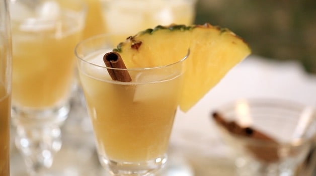 a glass of Christmas Punch garnished with a pineapple and cinnamon stick 