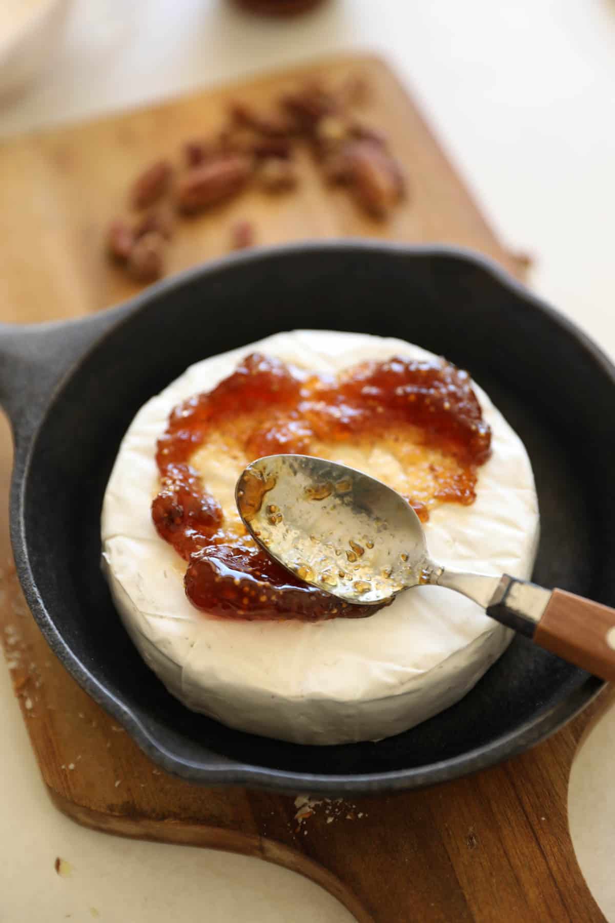a sppon spreading fig jam on brie