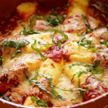 Cheese Manicotti in a terra cotta serving dish with fresh basil