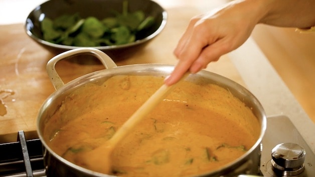 stirring spinach into sun-dried tomato sauce