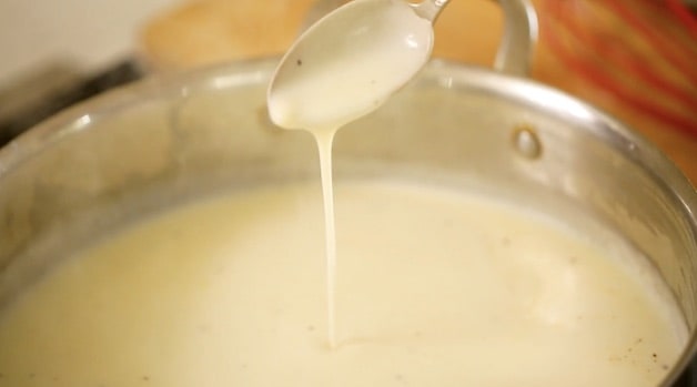 Bechamel Sauce dripping from a spoon in a skillet
