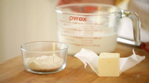 Bowl of flour, pitcher of milk and butter on a wooden cutting board