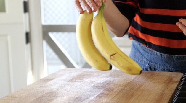 a person holding up two unripe bananas