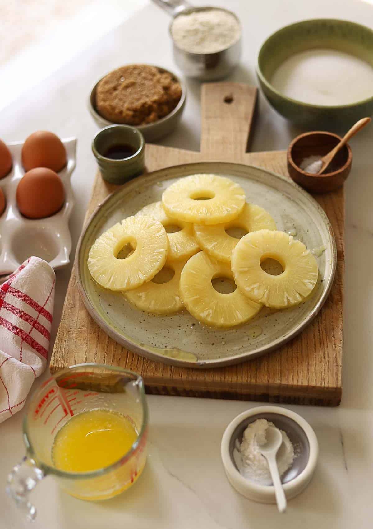 Pineapple rings, brown sugar, eggs, melted butter and dry ingredients on a counter.