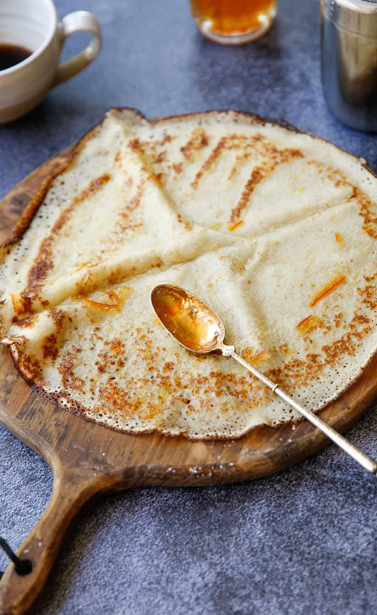 a cooked crepe on a wooden board with a spoon filled with orange marmelade