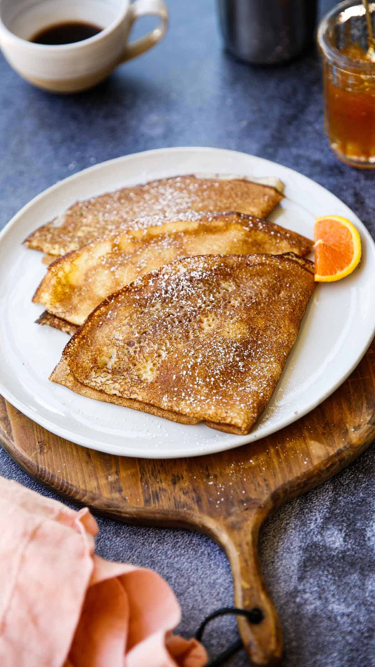 A board topped with 3 folded crepes with powdered sugar