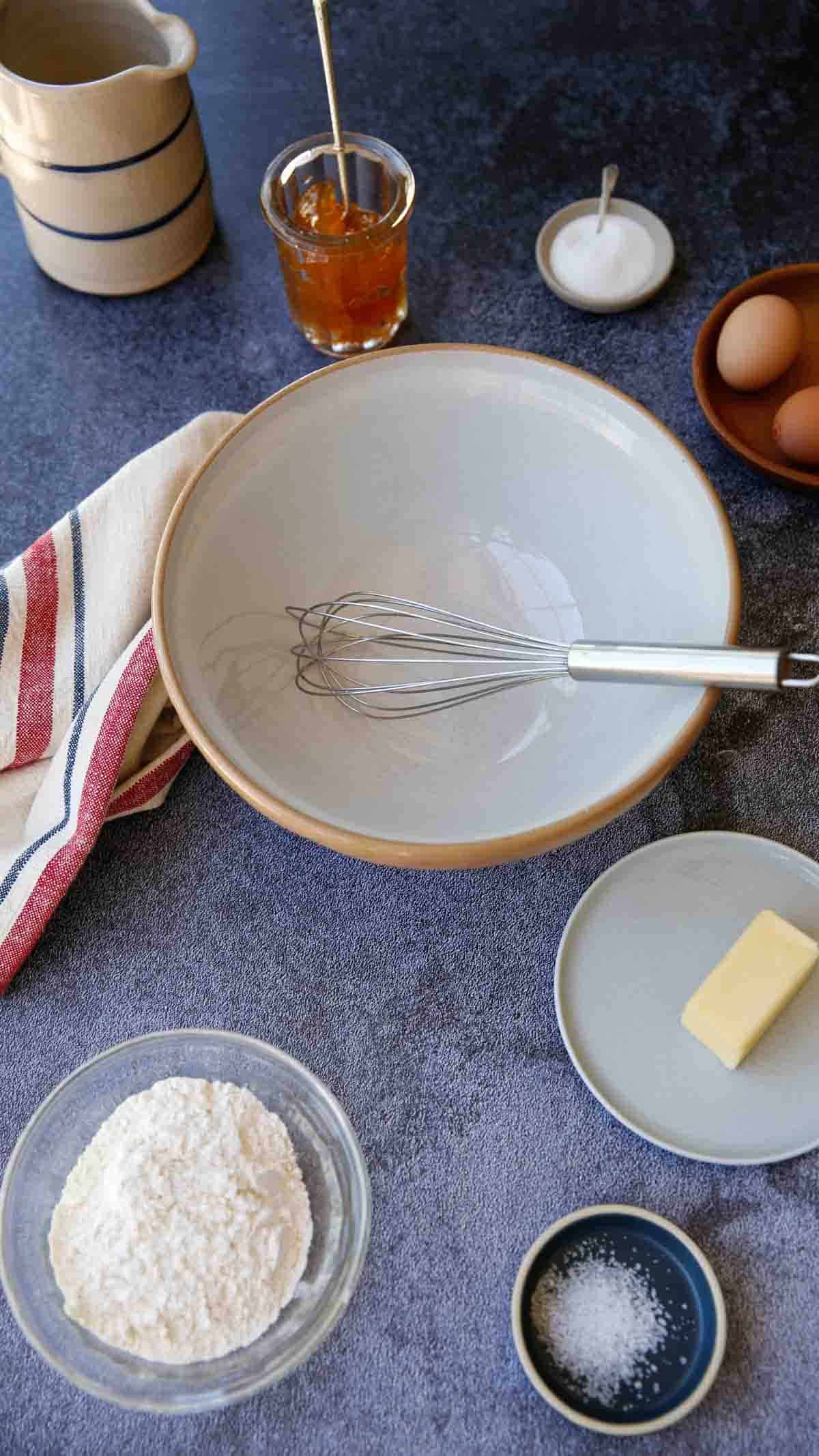 A mixing bowl and crepe ingredients spread out on a counter