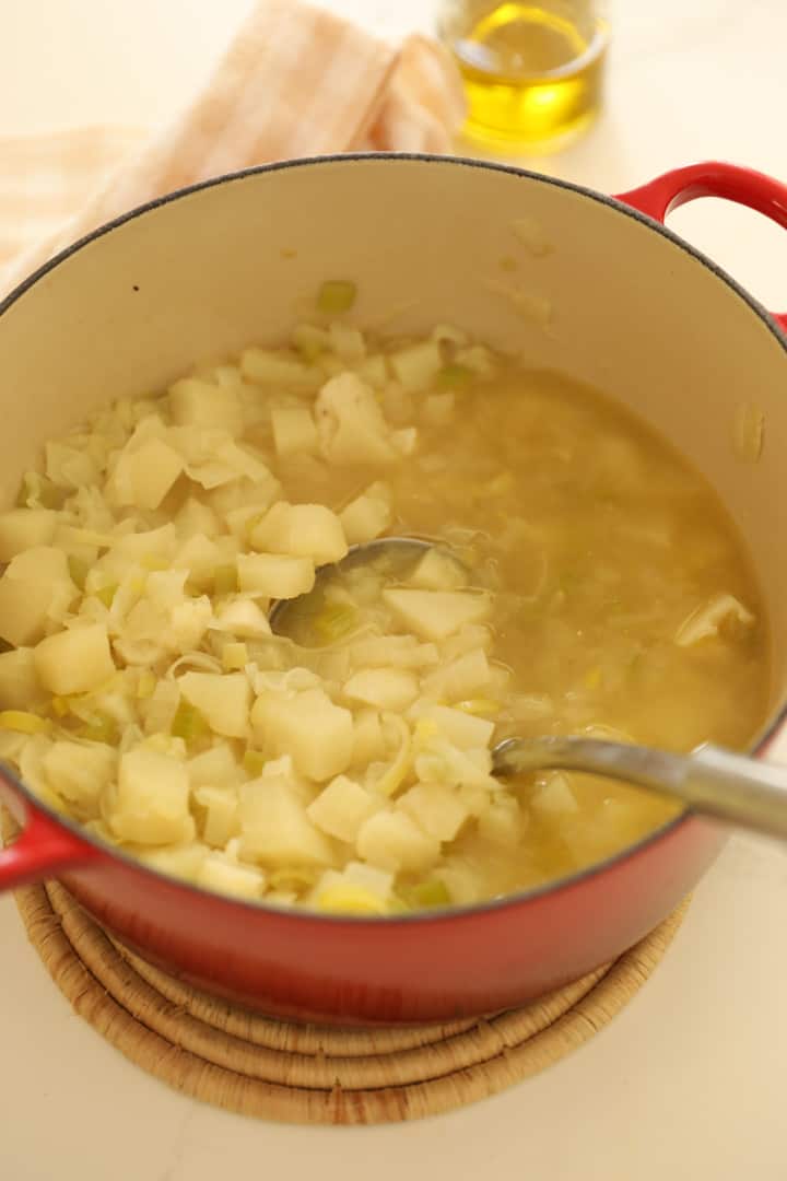 a red Dutch oven filled with tender potatoes, leeks and chicken broth