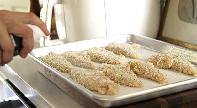 Spraying chicken tenders on a baking sheet with oil before air frying