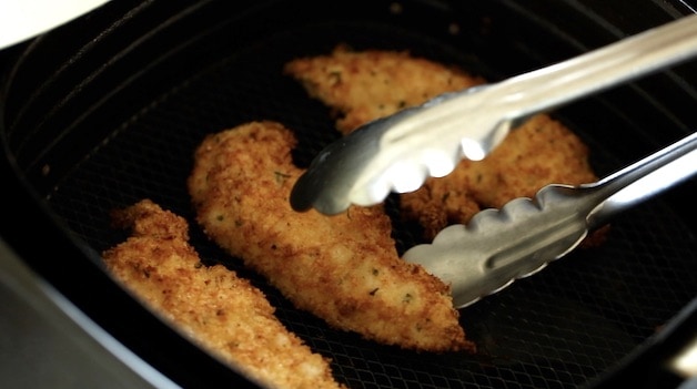 Cooked chicken tenders in air fryer with tongs removing them