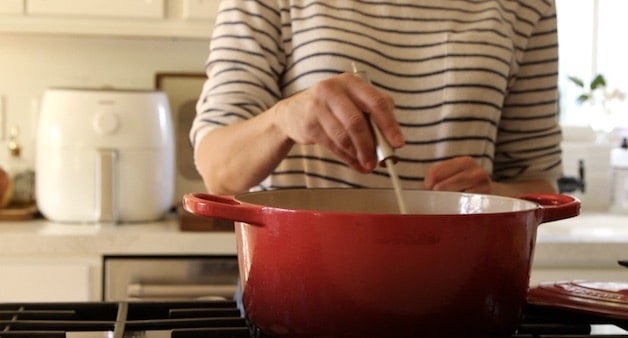A woman stirring soup with a ladle in a red pot