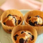 Three blueberry muffins made in the air fryer resting on a cake stand in parchment paper liners