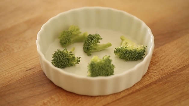 broccoli florets in the bottom of a mini white quiche dish