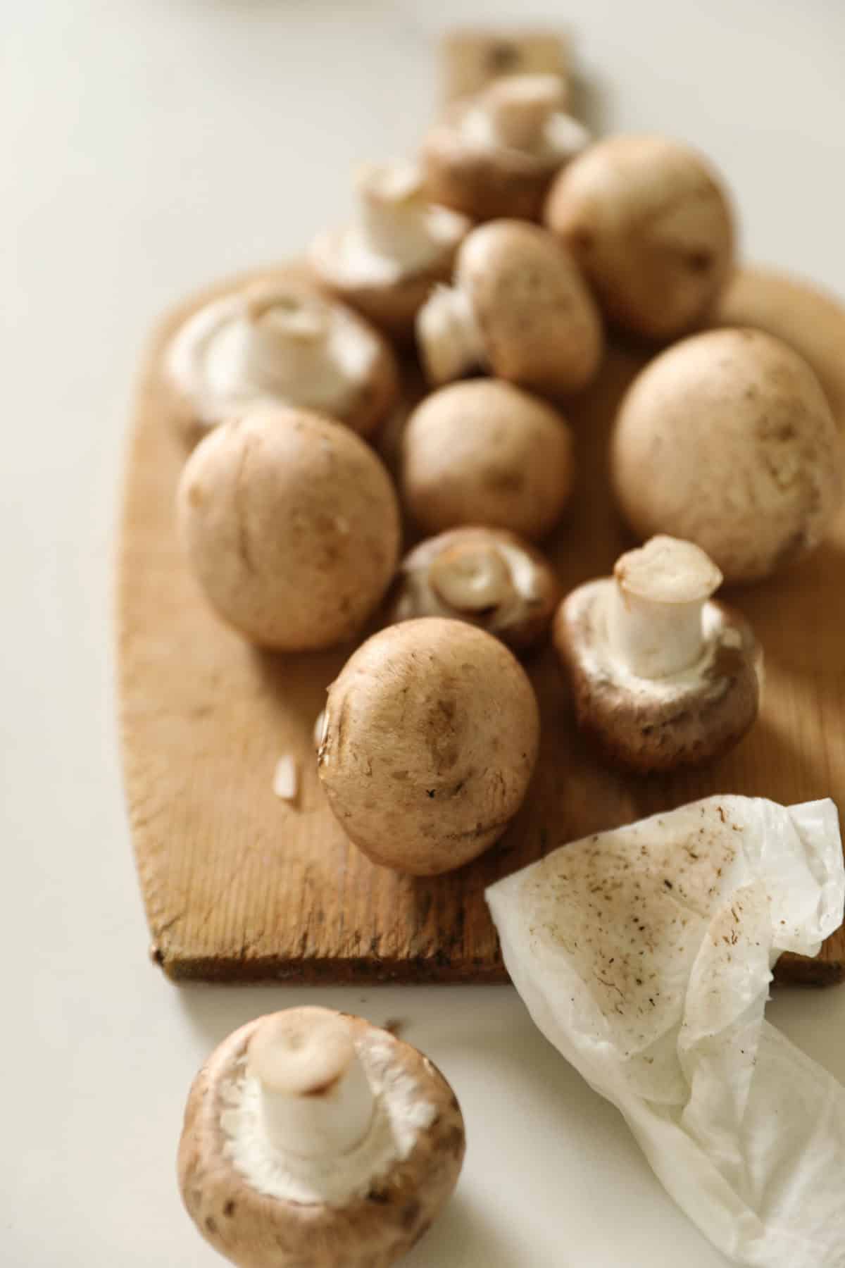 Cremini Mushrooms being cleaned with a paper towel on a cutti g board.