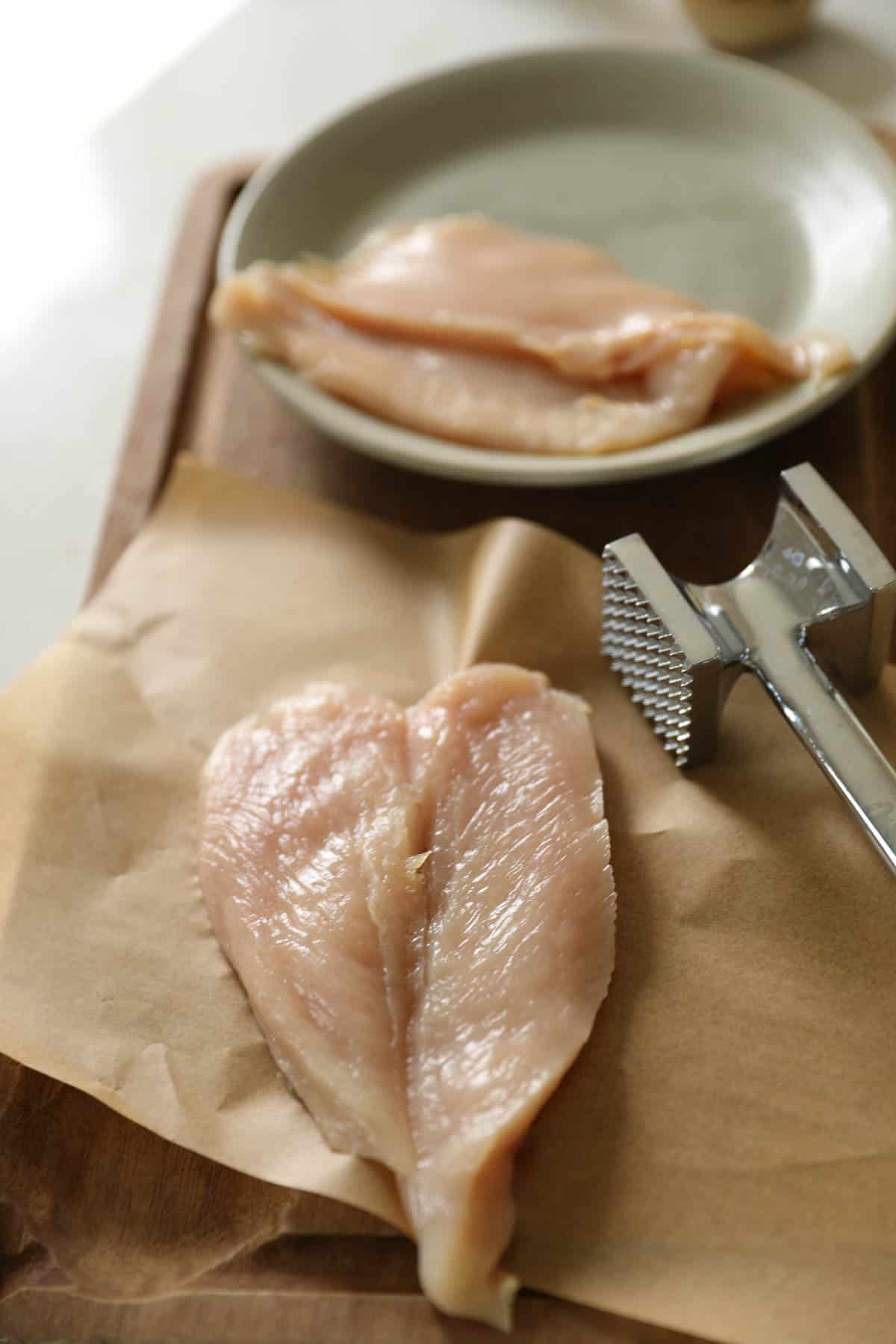 Chicken breast sliced in half and being pounded into cutlets.