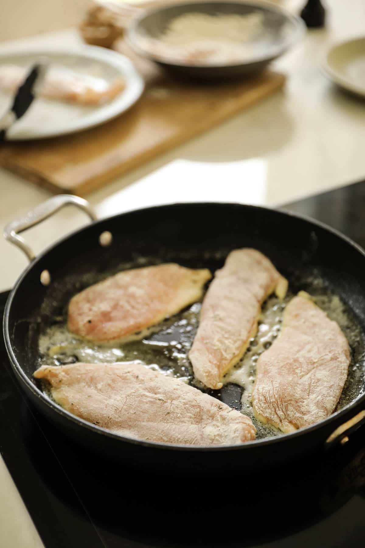 Chicken breasts sautรฉing in a large skillet.