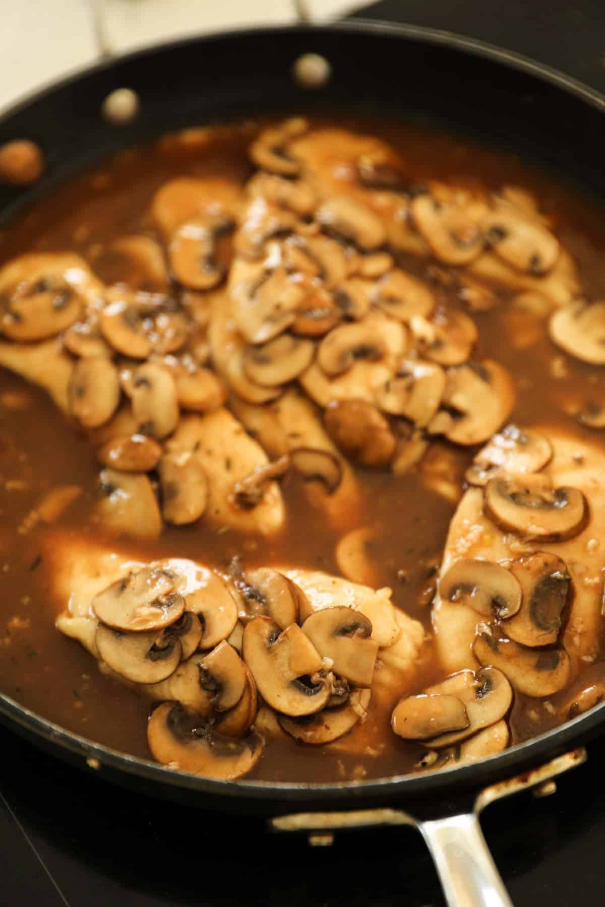 Chicken, mushrooms and marsala sauce simmering in a skillet.