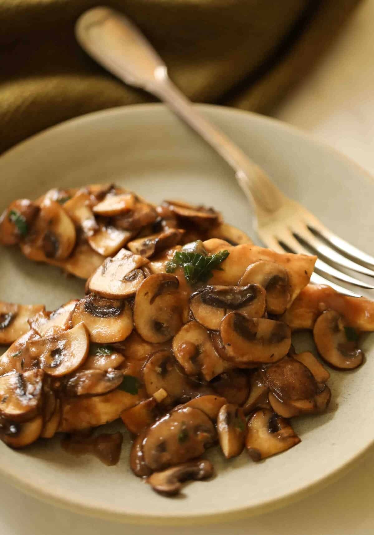 Two chicken breasts simmered in a mushroom wine sauce on a green plate.
