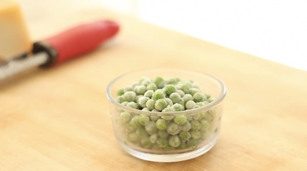a bowl of frozen peas on a cutting board