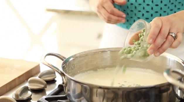 adding frozen peas to a skillet of sauce