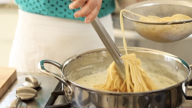 adding fettuccine noodles to sauce in skillet