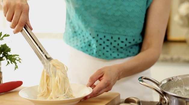 placing fettuccine in a bowl with tongs