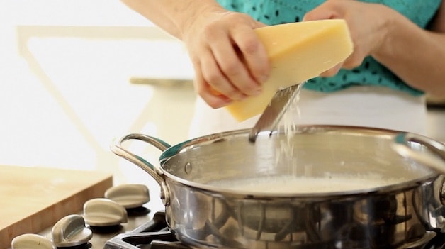 grating parmesean cheese to skillet of alfredo sauce