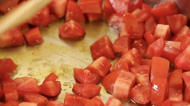 Diced tomatoes sautéing in a skillet with oil
