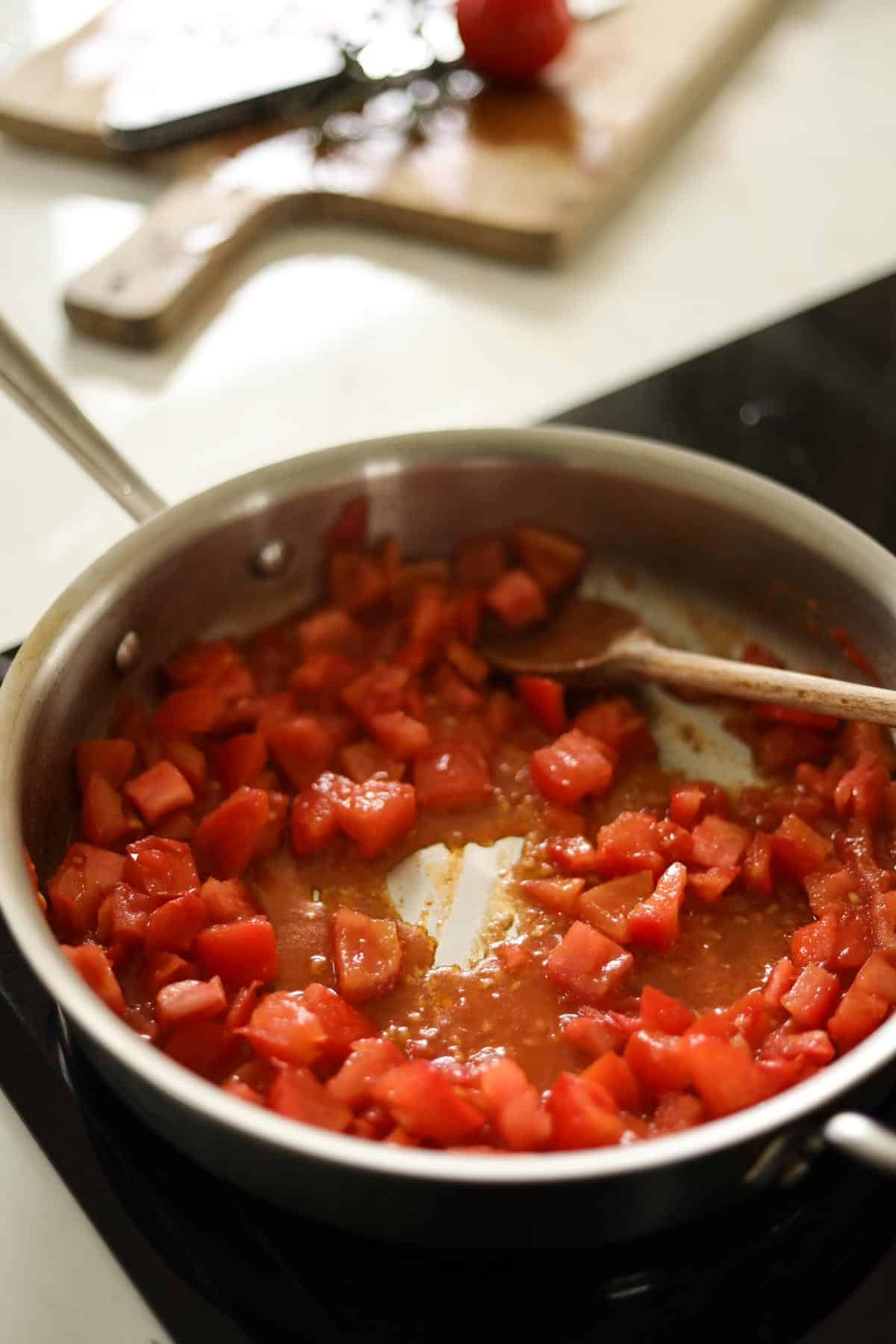 Diced tomatoes cooking in a skillet with a wooden spoon.