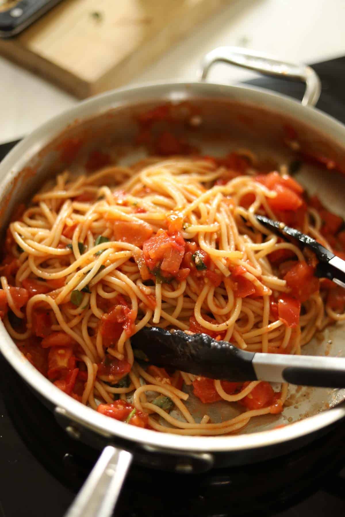 spaghetti pasta tossed in a skillet with tomatoes, basil and garlic.