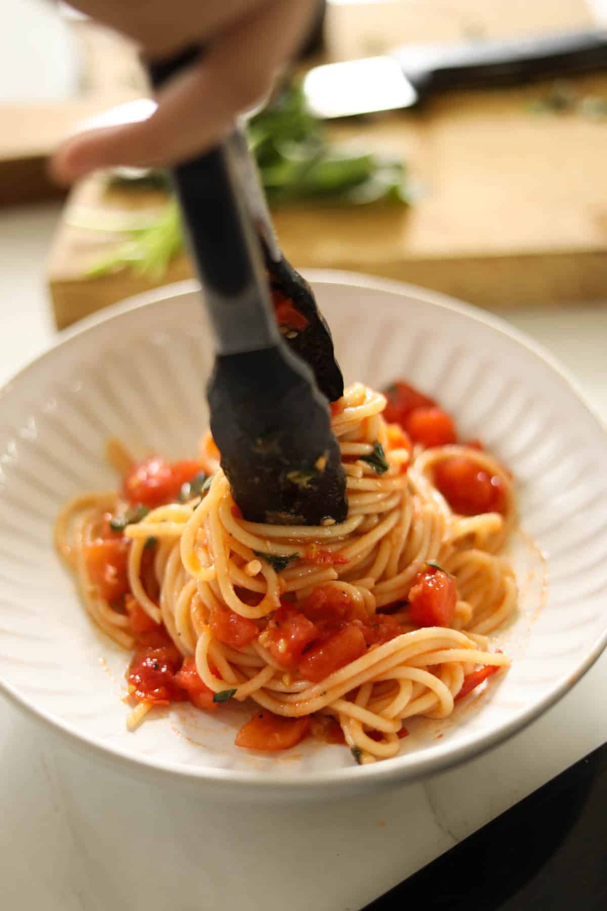pasta with tomato sauce being served in a bowl with tongs twisting the pasta into a nest.