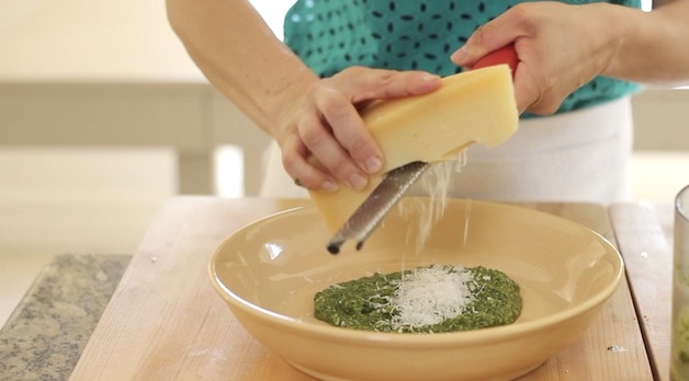 Grating Parmesan cheese into a bowl of pesto